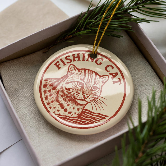 A round ornament with a cat image and the text "FISHING CAT" is displayed in a box, surrounded by pine branches.