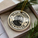 A round ornament with a black and white illustration of a dog's face, surrounded by text that reads "FLAT-COATED RETRIEVER".