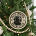 A Christmas tree decorated with ornaments, including a circular ornament with a black and white illustration of a retriever dog and the text "FLAT-COATED RETRIEVER" printed on it.