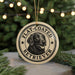 A round ornament featuring a black and white illustration of a retriever dog, with the text "FLAT-COATED RETRIEVER" printed on it.