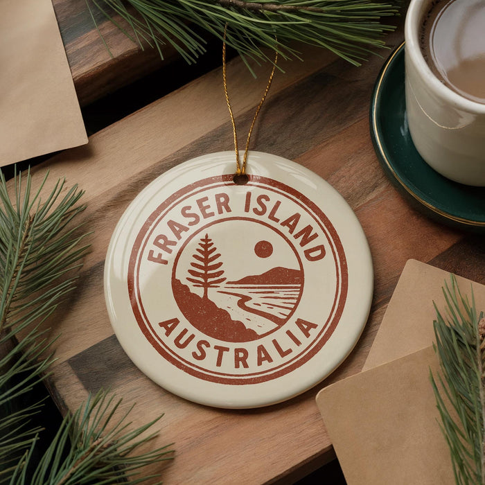 A circular ornament with the text "FRASER ISLAND AUSTRALIA" printed on it, surrounded by pine branches and a cup of coffee on a wooden surface.