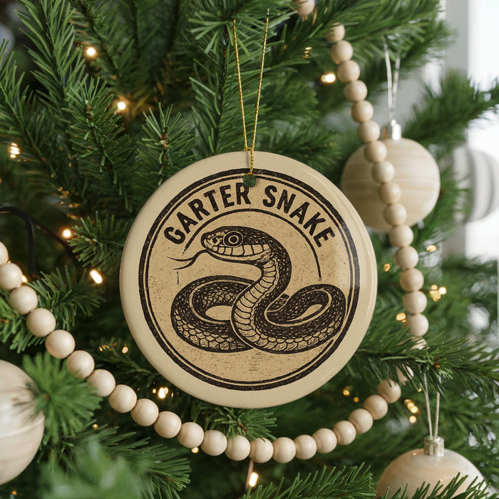 A round ornament with a snake design hangs from a Christmas tree, surrounded by other ornaments and lights.