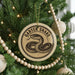 A round ornament with a snake design hangs from a Christmas tree, surrounded by other ornaments and lights.