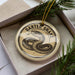 A circular ornament with a snake design, placed inside a box with pine branches.