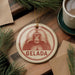 A circular ornament with a red and white design featuring a monkey's face, hanging on a wooden surface.