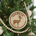 A circular ornament with a deer image and the word "Gereux" on it, hanging on a Christmas tree.