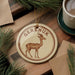 A circular ornament featuring a brown deer with antlers, hanging on a wooden surface.