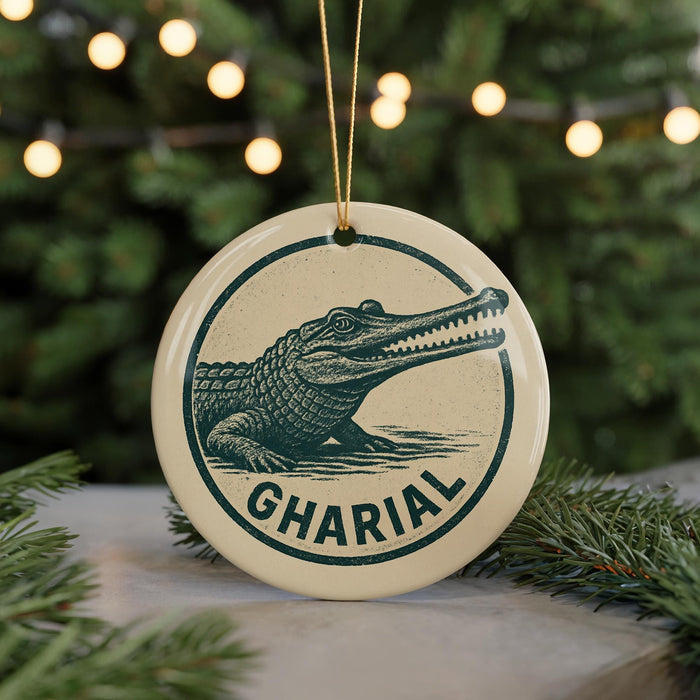 A ceramic ornament featuring a crocodile image and the word "GHARIAL" printed on it, placed on a surface with pine branches in the background.
