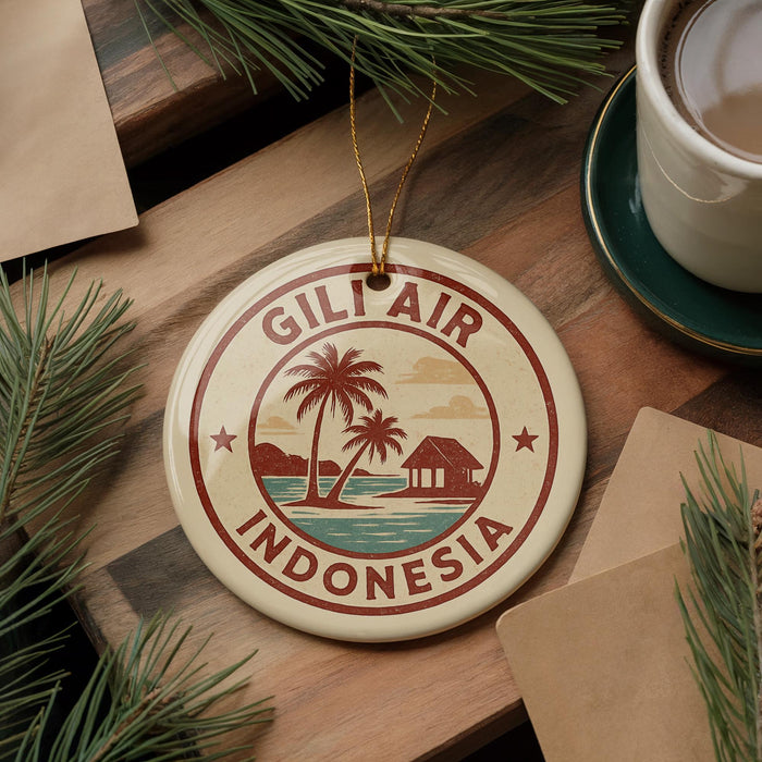 A round ornament with the text "GILI AIR INDONESIA" and a palm tree design, placed on a wooden surface next to a cup of coffee and some pine branches.