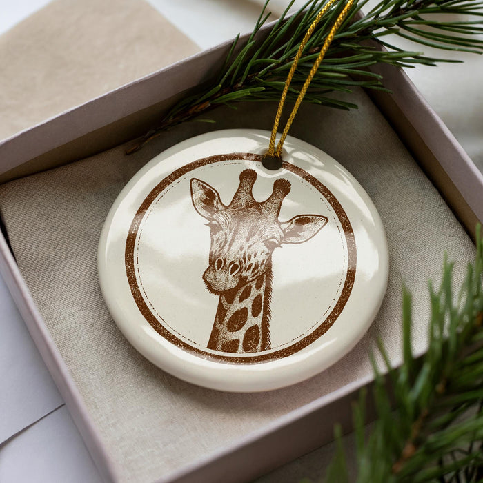 A ceramic ornament in the shape of a giraffe is displayed in a box, surrounded by pine branches.