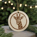 A round ornament featuring a giraffe's head is displayed against a blurred background of a Christmas tree with twinkling lights.