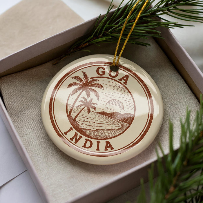 A circular ornament with the text "Goa India" printed on it, surrounded by a decorative element resembling a palm tree and a sunset.