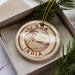 A circular ornament with the text "Goa India" printed on it, surrounded by a decorative element resembling a palm tree and a sunset.