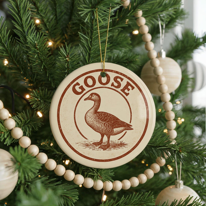 A Christmas tree decorated with ornaments, including a circular ornament with a goose design and the word "GOOSE" written on it.