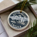 A decorative ornament in a box, featuring a circular design with illustrations of Gothenburg, Sweden, and a bridge.