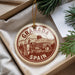 A circular ornament with the text "GRANADA SPAIN" printed on it, hanging from a string.