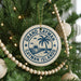 A circular ornament on a Christmas tree, featuring the text "GRAND CAYMAN ISLANDS" surrounded by a palm tree and a beach scene.