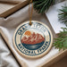 A decorative ornament with the text "GRAND Teton NATIONAL FPAARK" and a mountain landscape design, hanging from a string.