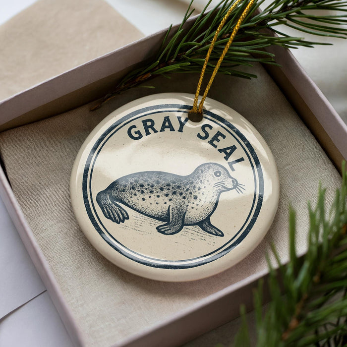 A circular ornament with a seal image and the text "GRAY SEAL" on it, placed in a box with pine branches.