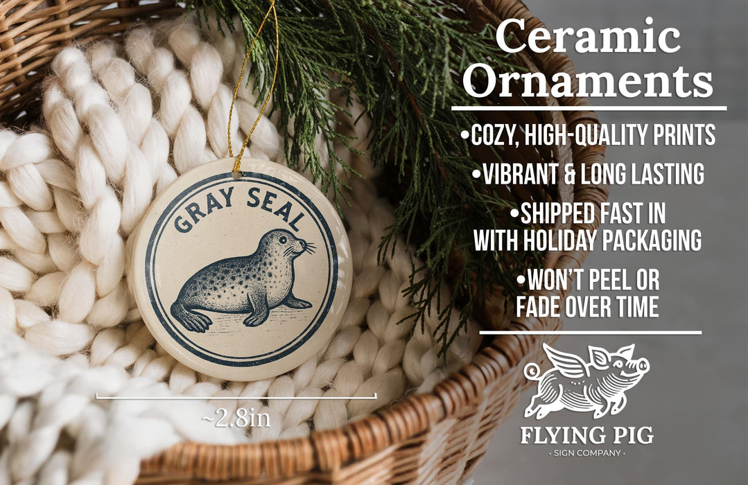 a ceramic ornament with a gray seal design, hanging from a wicker basket. The ornament is described as a "Ceramic Ornaments" and is described as "Cozy, High-quality Prints" and "Vibrant & Long Lasting". It is also noted that the ornament is "Shipped Fast in with Holiday Packaging" and " Won't Peel or Fade Over Time". The image is a close-up of the ornament, and the text provides information about the ornament's features and benefits.