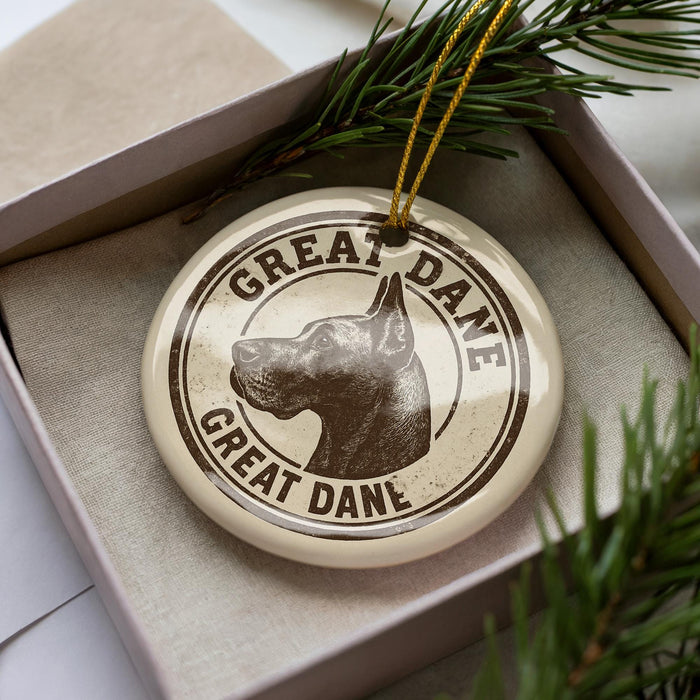 A circular ornament with the text "GREAT DANEL" and a dog's head image, placed inside a box with pine branches.