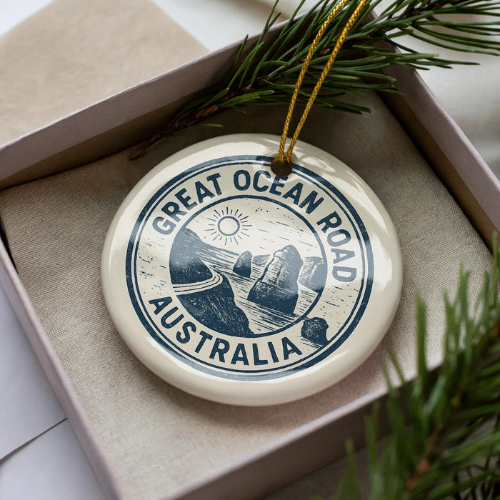 A circular ornament with the text "GREAT OCEAN ROAD AUSTRALIA" printed on it, placed inside a box with pine branches.