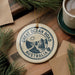 A circular ornament with the text "GREAT OCEAN ROAD AUSTRALIA" printed on it, surrounded by pine branches and a cup of coffee on a wooden surface.