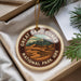 A circular ornament with a design of sand dunes and mountains, hanging from a string.