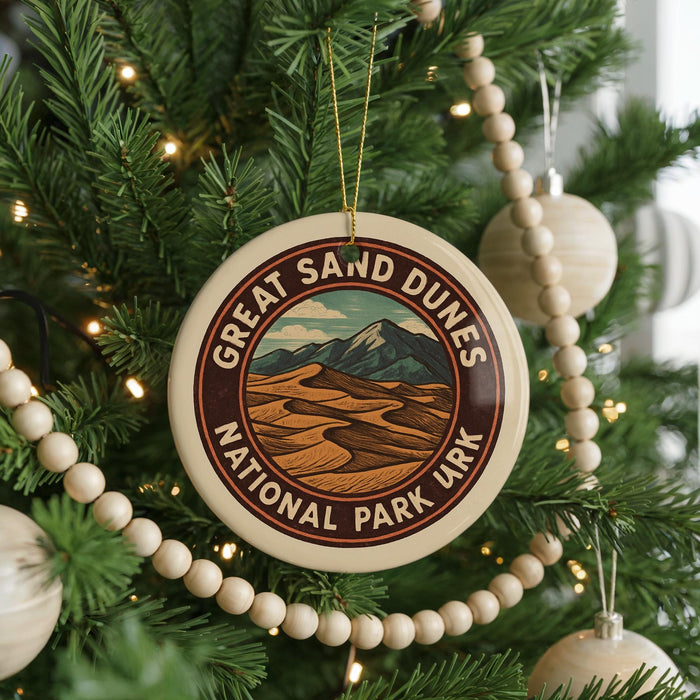 A circular ornament on a Christmas tree, featuring a design of sand dunes and mountains, with the text "GREAT SAND DUNES NATIONAL PARK URK" around the edge.