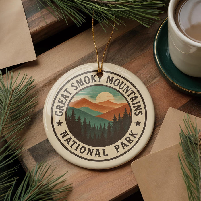 A circular ornament with the text "GREAT SMOK MOUNTAINS NATIONAL PARK" is displayed on a wooden surface, surrounded by pine branches and a cup of coffee.