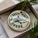 A circular ornament with the text "GREAT WHITE SHARK" and a graphic of a shark is displayed in a box, surrounded by pine branches.
