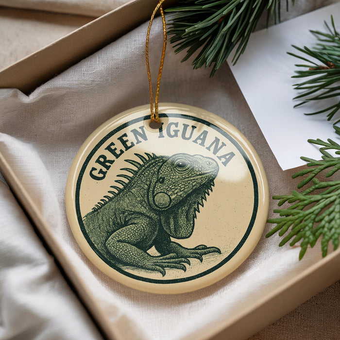 A circular ornament featuring a green iguana, with the text "GREEN IGuana" printed on it, is displayed in a box with pine branches.