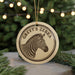 A circular ornament featuring a zebra's head, with the text "GREVY'S ZEBRA" printed on it, is displayed in front of a blurred Christmas tree.