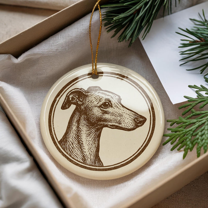 A round ornament featuring a dog's head is displayed in a box, surrounded by pine branches and a white card.