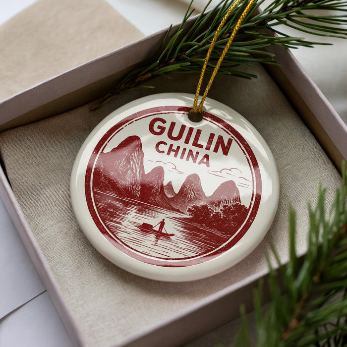 A decorative ornament in a box, featuring a red and white design with mountains and a boat, and the text "GUILIN CHINA".