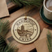 A circular ornament with the text "HANGHOU CHINA" and an illustration of a pagoda, surrounded by pine branches and a cup of coffee on a wooden surface.