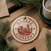 A circular ornament with the text "HARARE ZIMBABWE" printed on it, surrounded by pine branches and a cup of coffee on a wooden surface.
