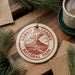 A circular ornament with the text "HAWAII'I VOLCANOES NATIONAL PARK" printed on it, surrounded by pine branches and a cup of coffee on a wooden surface.