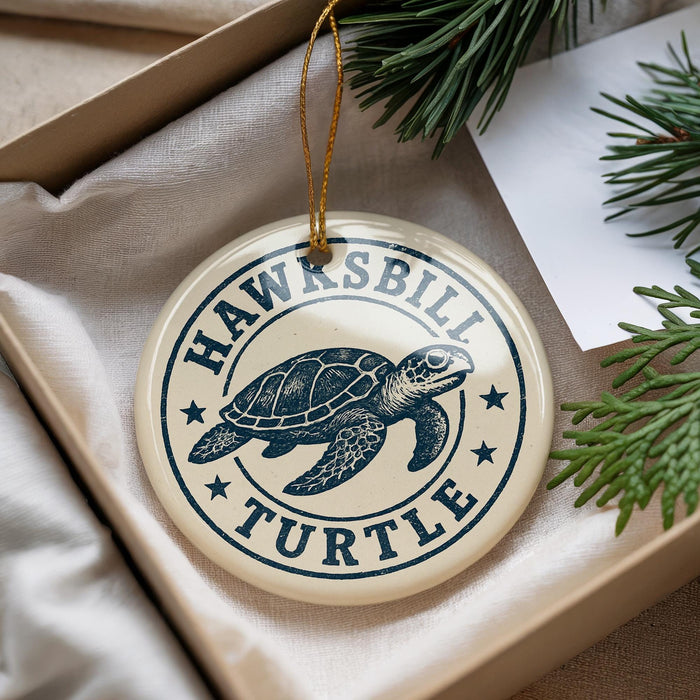 A circular ornament with a turtle design, featuring the text "HAWKSBILL TURTLE" on it, is displayed in a box with pine branches.