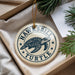 A circular ornament with a turtle design, featuring the text "HAWKSBILL TURTLE" on it, is displayed in a box with pine branches.