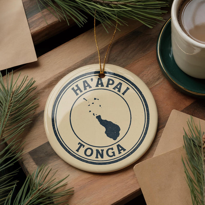 A circular ornament with the text "HA'APAI TONGA" and a map of Tonga, placed on a wooden surface next to a cup of coffee and pine branches.