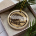 A ceramic ornament in the shape of a porcupine, with a brown and beige color scheme, is displayed in a box with pine branches.
