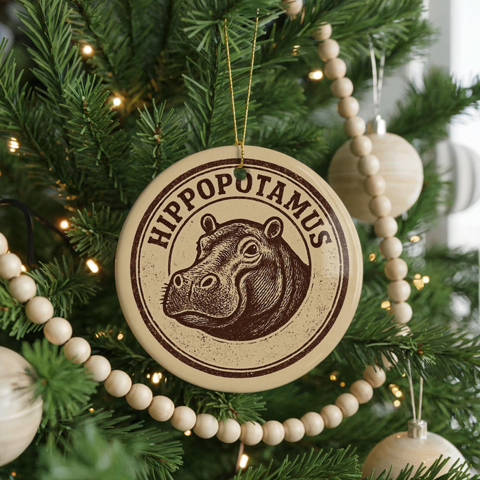 A circular ornament with a hippopotamus image is hanging on a Christmas tree, surrounded by beaded ornaments and twinkling lights.
