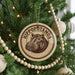 A circular ornament with a hippopotamus image is hanging on a Christmas tree, surrounded by beaded ornaments and twinkling lights.