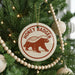 A Christmas tree decorated with ornaments, including a circular ornament with a picture of a badger and the text "HONEY BADGER" on it.