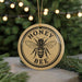 A round ornament with the text "HONEY BEE" and a bee illustration, hanging from a string.