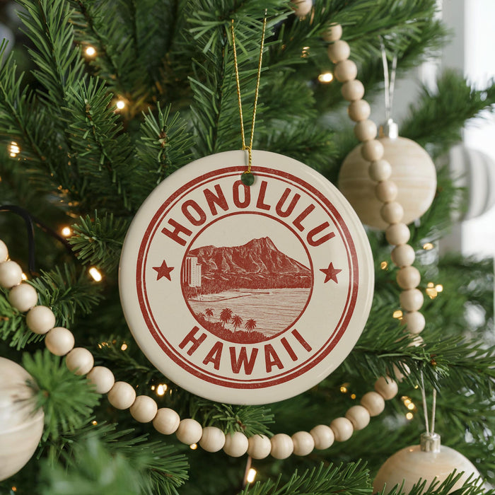 A circular ornament on a Christmas tree with the text "HAWAII" in red and white, featuring a mountain and beach scene.