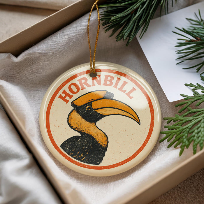 A round ornament with a hornbill illustration is displayed in a box, surrounded by pine branches.