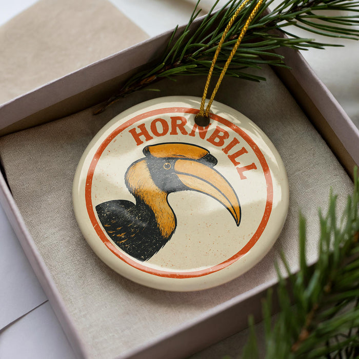 A round ornament with a hornbill illustration on it, placed in a box with pine branches.