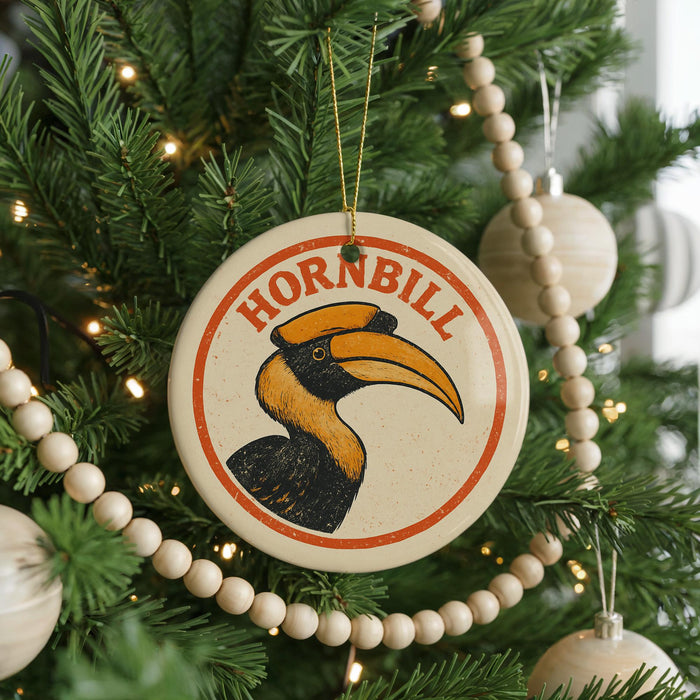 A circular ornament with a hornbill illustration is hanging on a Christmas tree, surrounded by ornaments and lights.